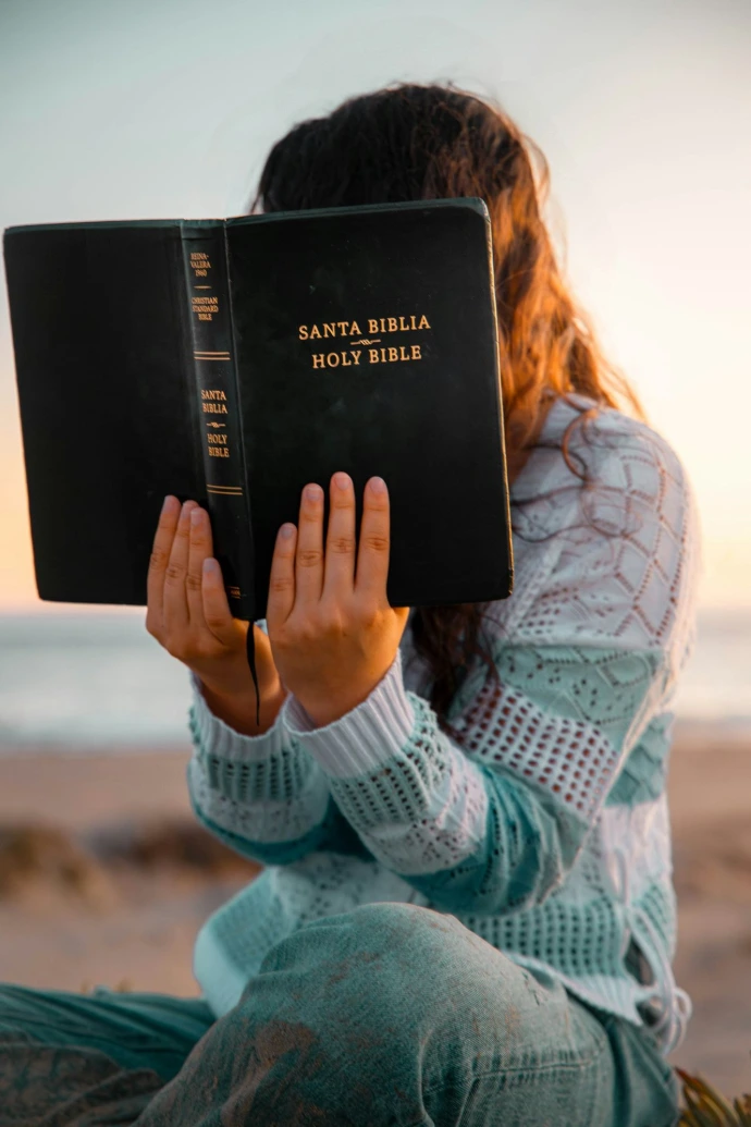 Woman holds a bible in front of her face.